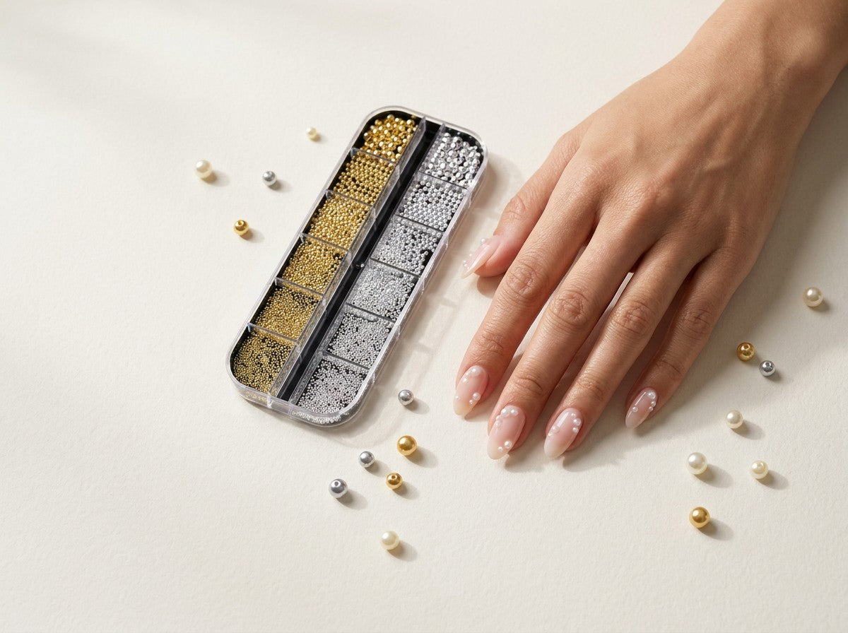 Hand mit Perlen auf den Nägeln, daneben Gold- und Silberperlen