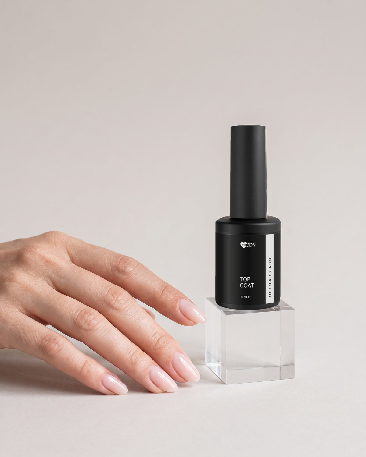 Hand mit glänzenden Nude-Nägeln neben Top Coat Ultra Flash