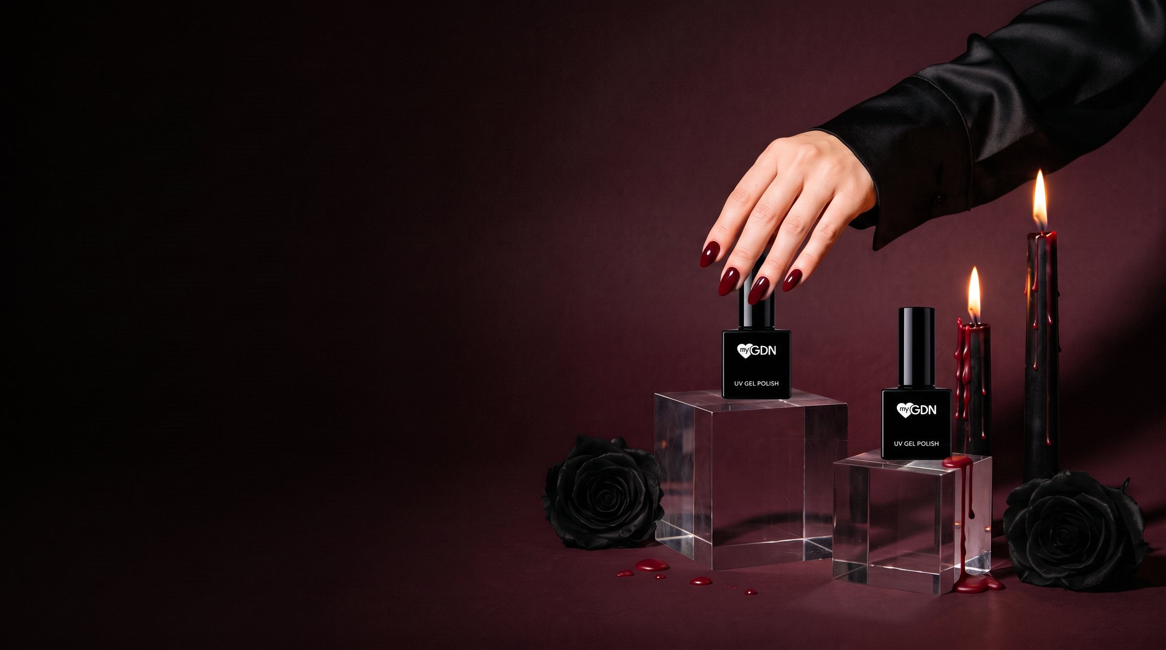 Hand mit weinroten Rouge-Noir-Nägeln an zwei myGDN Shellac-Flaschen, dazu schwarze Kerzen mit rotem Wachs und schwarze Rosen
